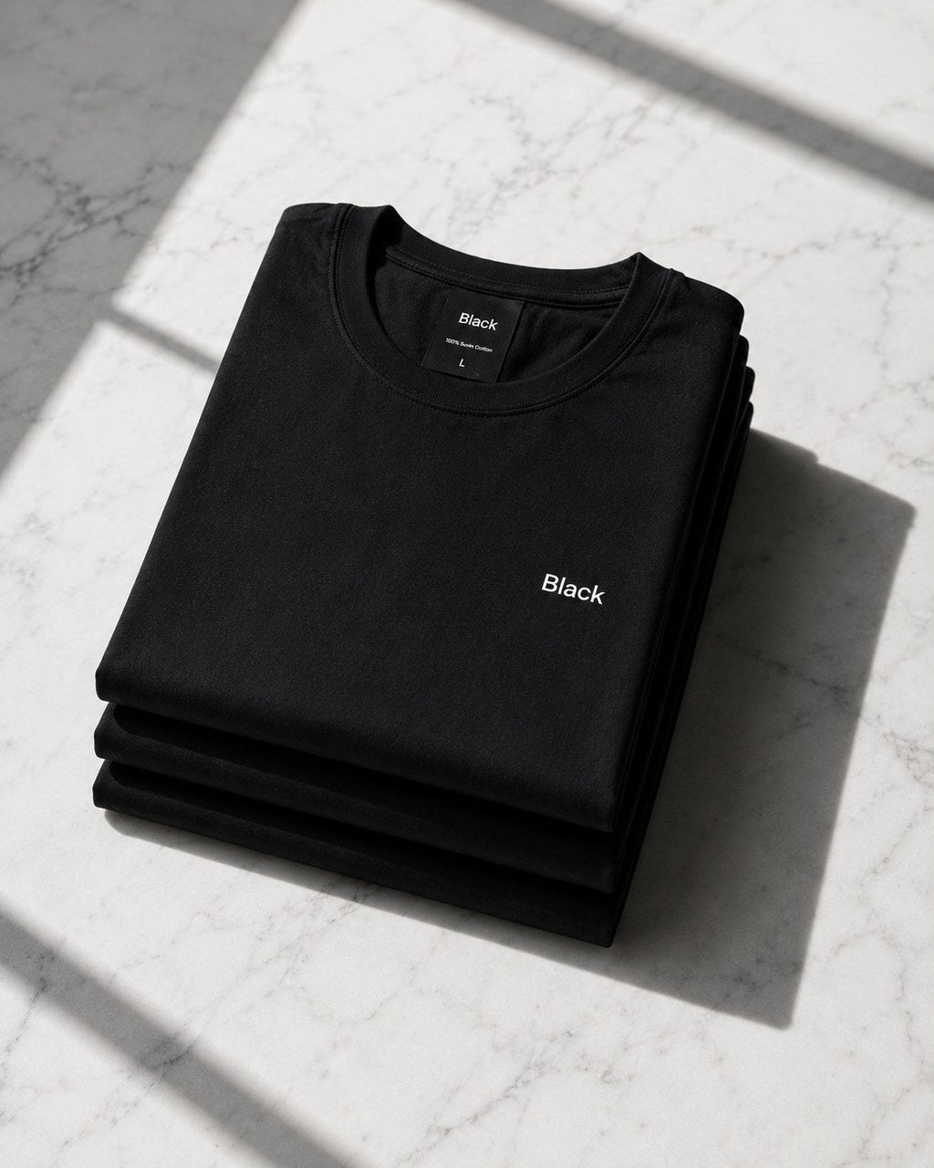 Stack of folded Black tees on marble in sunlight