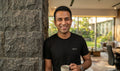 Man wearing the Black tee, smiling with a coffee