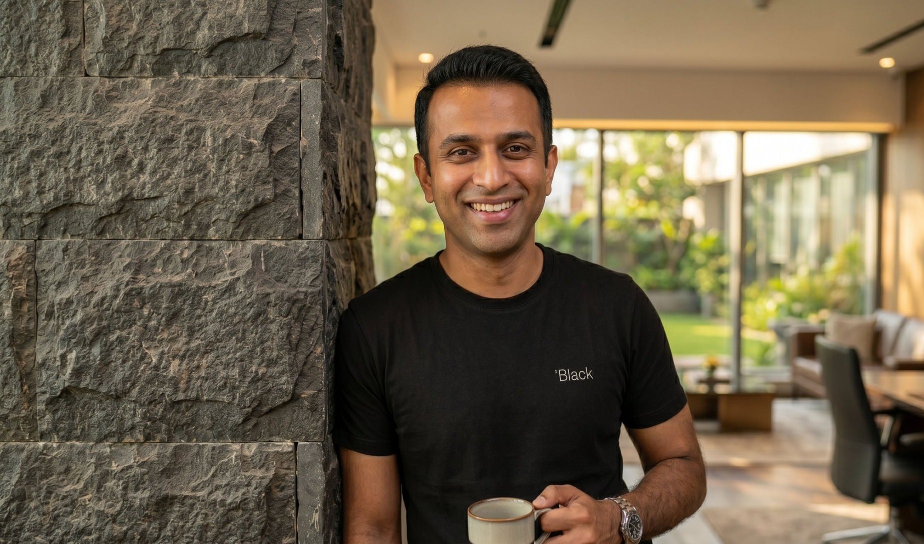 Man wearing the Black tee, smiling with a coffee
